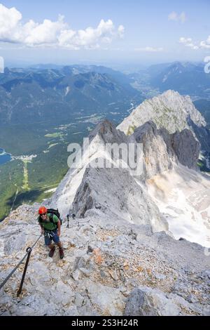 Alpinista con casco in ferrata, Zugspitz via ferrata, salita allo Zugspitze, vista della cresta di montagna con Waxenstein e Riffelspit Foto Stock