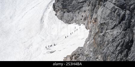 Alpinisti in coda al passaggio dall'Hoellentalferner allo Zugspitz via ferrata, su un campo innevato, overturismo, bacino montano con ghiacciaio Foto Stock