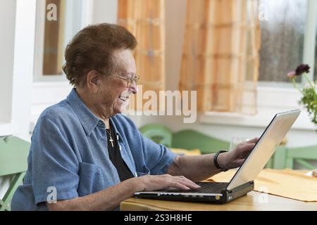 Una donna anziana con laptop scrive e-mail Foto Stock