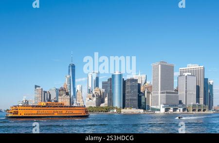 Skyline di Lower Manhattan con il traghetto Staten Island in primo piano, incorniciato da One World Trade Center, Battery Park e un motoscafo in una giornata limpida. Foto Stock