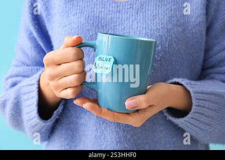Donna che tiene una tazza e una bustina di tè con testo BLU LUNEDÌ, primo piano Foto Stock
