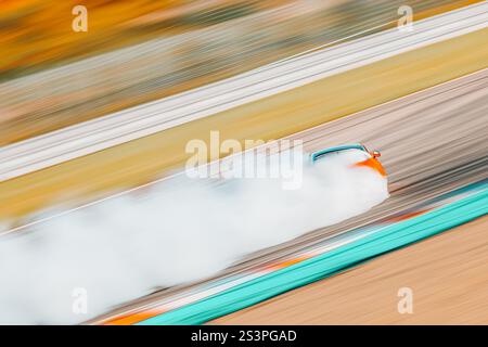 Panning dinamico di un'auto alla deriva su un circuito da corsa, circondato da un intenso fumo proveniente dalle gomme in fiamme, oscurando parzialmente il veicolo. Il mot Foto Stock