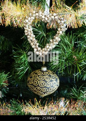 Un albero di Natale con una decorazione a forma di cuore e un ornamento glitterato nero e oro e una tinsel d'oro appesa ad esso Foto Stock