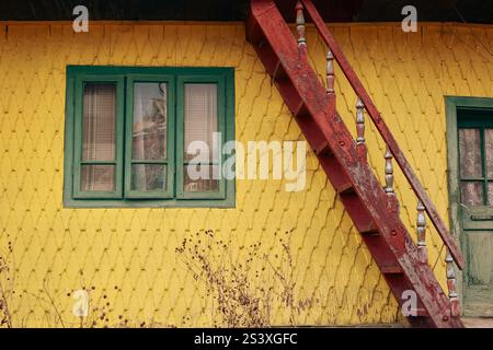 Facciata esterna di una vecchia casa interamente in legno. La casa colorata: Gialla ma le finestre verdi, rosse. xix - xx secolo. Bicaz, Romania Foto Stock