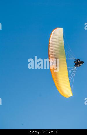 il vivace parapendio arancione si libra attraverso un cielo blu limpido. Foto Stock