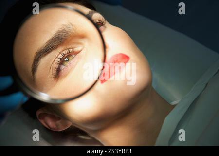 Medico la mano che tiene la lente di ingrandimento su Donna's Eye Foto Stock
