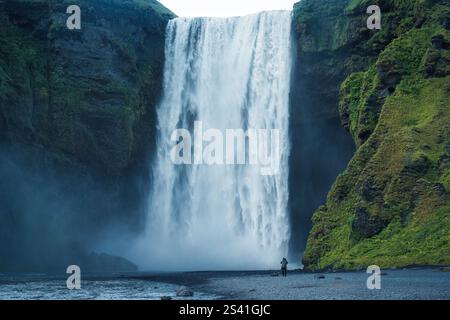 Maestosa cascata Moody Skogafoss che scorre in lussureggiante montagna durante l'estate a sud dell'Islanda Foto Stock