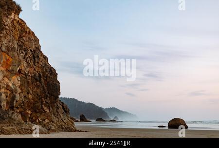 Scogliera costiera con un oceano sereno e un orizzonte nebbioso al crepuscolo Foto Stock