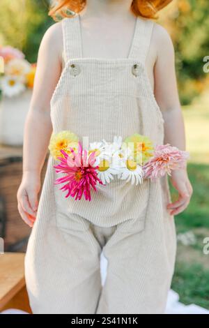 Bambino che indossa tute beige con fiori colorati in tasca all'esterno. Foto Stock