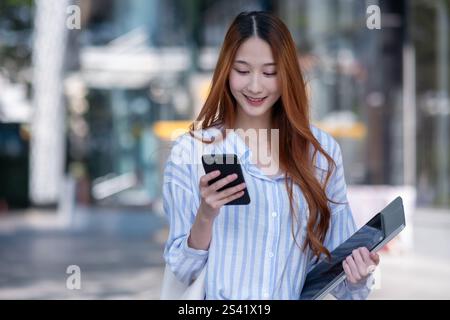 La donna ha un cellulare e un tablet. Sta sorridendo. Sta camminando per strada Foto Stock