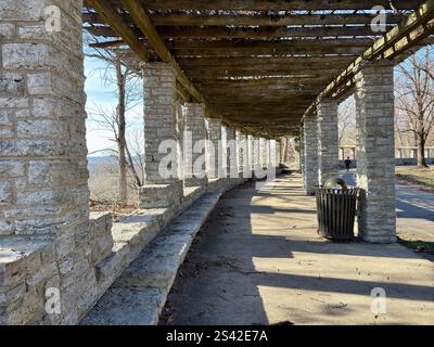 Pergola in pietra con travi in legno e ombre su un sentiero lastricato in un parco Foto Stock