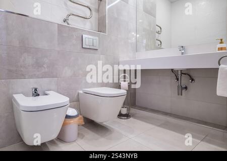 Un bagno pulito e contemporaneo con doccia in vetro, WC a parete, scaldasalviette e piastrelle in stile marmo. Foto Stock