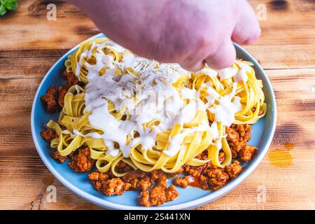 Spaghetti alla bolognese nidificano con salsa besciamella e manzo macinato fritto con pomodori, cipolle e carote su un piatto blu su un tavolo di legno. Vie superiori Foto Stock