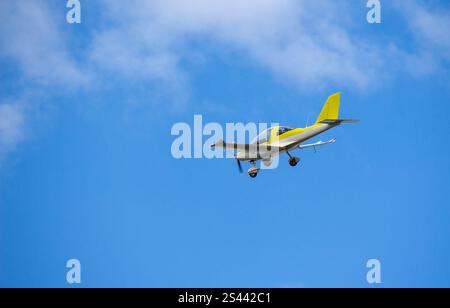 Un aereo bianco e giallo microchiaro che vola su un cielo blu con nuvole bianche sullo sfondo Foto Stock