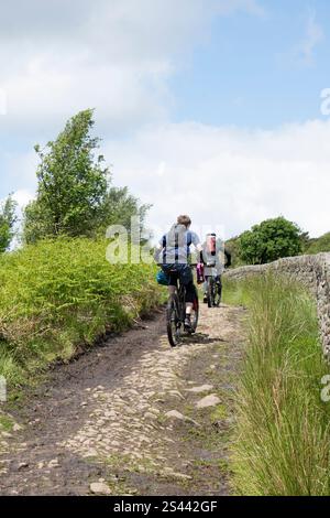 Due ciclisti su una pista sterrata che conduce attraverso il paesaggio brughiero della riserva naturale di Blacka Moor, Peak District, Regno Unito Foto Stock