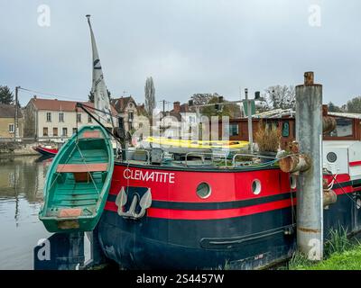 Una casa galleggiante colorata chiamata Clemattite attraccata lungo un fiume tranquillo in una tranquilla cittadina circondata da alberi ed edifici rustici in una giornata nuvolosa Foto Stock
