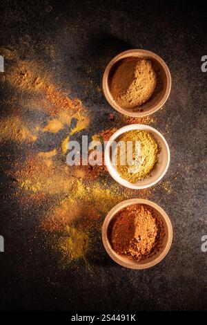 Tre piattini con spezie colorate e luminose su un tavolo nero, piatto Foto Stock