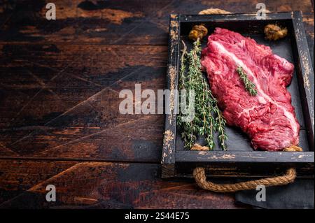 Tenera bistecca di manzo non cotta appesa, bistecca appendiabiti in vassoio di legno con erbe aromatiche. sfondo in legno. vista dall'alto Foto Stock