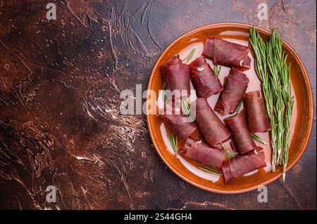 Tipica carne spagnola secca cecina, jamon di manzo spagnolo su piatto con rosmarino. sfondo marrone. vista dall'alto. Foto Stock