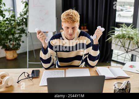 Giovane professionista in un pullover a righe si concentra sul lavoro al suo portatile in mezzo al verde. Foto Stock