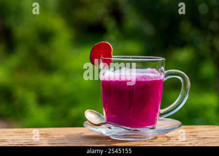 Latte di barbabietola rosa ottenuto da succo di barbabietola fresco mescolato con vaniglia e latte in una tazza trasparente sul tavolo in una caffetteria sullo sfondo naturale, primo piano, copia Foto Stock