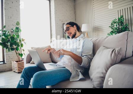 Giovane uomo che usa il computer portatile sul divano in un soggiorno luminoso e accogliente Foto Stock