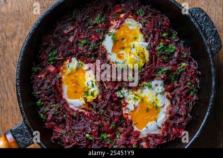 Barbabietole rosse bollite con uova fritte, peperoni rossi, cipolle e aneto verde in una padella su un tavolo di legno, vista ravvicinata dall'alto. Background alimentare. Sano f Foto Stock