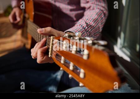 Vista ravvicinata delle mani che suonano una chitarra acustica. L'illuminazione enfatizza la struttura in legno dello strumento e cattura la creatività e il relax Foto Stock