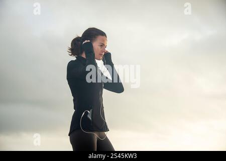 jogger donna che regola le cuffie, all'aperto Foto Stock