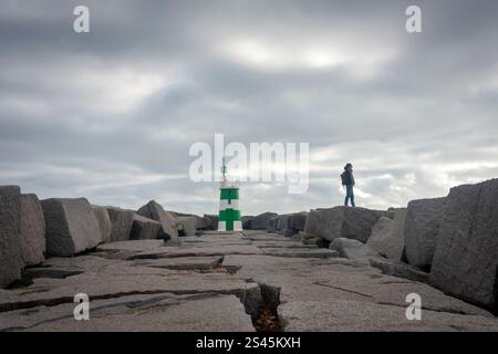donna in piedi sulle rocce accanto a un faro su una strada rialzata Foto Stock