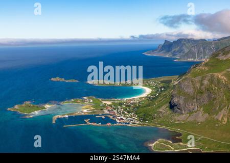 Vista aerea di una spiaggia incontaminata e di un villaggio a Lofoten, Norvegia, in una giornata di sole. Le acque blu-verdi brillano sotto il sole, con montagne lungo il Foto Stock