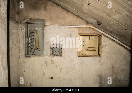 Un primo piano dettagliato dei collegamenti elettrici abbandonati in una casa abbandonata, che mostra fili esposti, raccordi corrosi e pareti vecchie. Questa immagine evoca temi di abbandono, decadenza e obsolescenza industriale, ideale per progetti incentrati sull'esplorazione urbana, sulle infrastrutture dimenticate o sulla fotografia concettuale Foto Stock