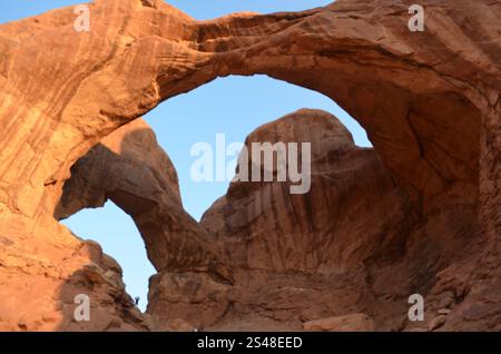 Enormi archi di roccia rossa si innalzano in rilievo contro un cielo blu in un'area desertica, mostrando splendide formazioni geologiche all'Arches National Park, Utah. Foto Stock