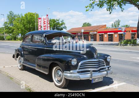 Un'auto d'epoca nera è parcheggiata in un parcheggio vicino a una strada con alberi e negozi circostanti, Chevrolet, Ilsede, quartiere Peine, bassa Sassonia, tedesco Foto Stock