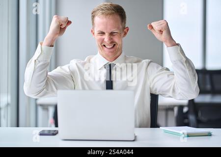 Felice giovane imprenditore online che guarda un notebook che celebra il successo. Foto Stock