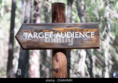 Un cartello di legno mostra la frase target audience, adagiata su uno sfondo di alberi alti in una tranquilla area forestale durante il giorno. Foto Stock