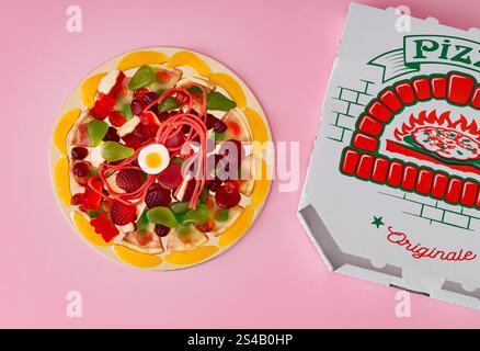 Layout creativo realizzato con un mix di caramelle gommose colorate su sfondo rosa pastello chiaro. Concetto minimalista di pizza dolce. Un'idea di pizza surreale alla moda. Foto Stock