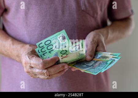 Primo piano di un uomo che conta 100 banconote in dollari australiani. Concetto di denaro contante: Salari, pagamenti, dividendi, investimenti, prestiti o vincite. Foto Stock