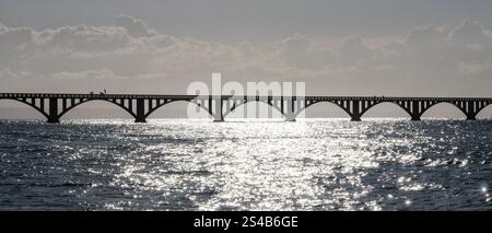 Un bellissimo ponte si estende graziosamente su un sereno corpo d'acqua, con il sole caldo che splende brillantemente su di esso, creando una vista pittoresca Foto Stock