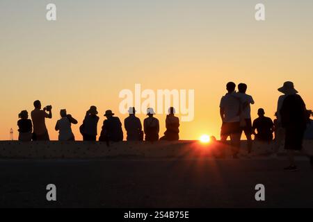 Una linea di persone che si stagliano contro un tramonto infuocato, catturando gli ultimi raggi di luce con le telecamere e l'apprezzamento silenzioso. Foto Stock