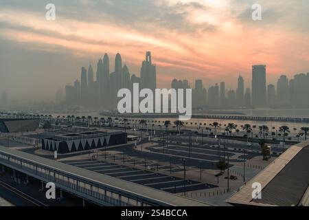 Il sole tramonta sull'iconico skyline di Dubai, avvolto da una nebbia mistica che ammorbidisce i grattacieli torreggianti e crea un ambiente sereno, quasi surreale Foto Stock