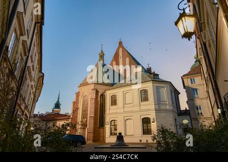 Il caldo bagliore dell'ora d'oro illumina un'affascinante piazza della chiesa in una città europea. La facciata della chiesa e gli edifici circostanti sono bagnati Foto Stock