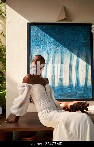 Persona nera fluida di genere ambigua in elegante abito bianco siede in una villa soleggiata. Tema per matrimoni LGBTQ, moderna moda da sposa. Festeggiamo Foto Stock