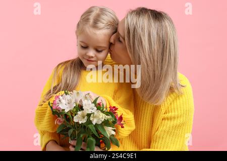 Donna con la figlia e bouquet di fiori di alstroemeria su sfondo rosa. Festa della mamma Foto Stock