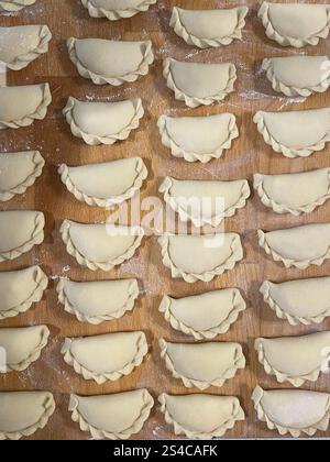 Gnocchi crudi su fondo di legno, cosparsi di farina. Una mano che tiene un gnocco in primo piano. Copia spazio. Foto Stock