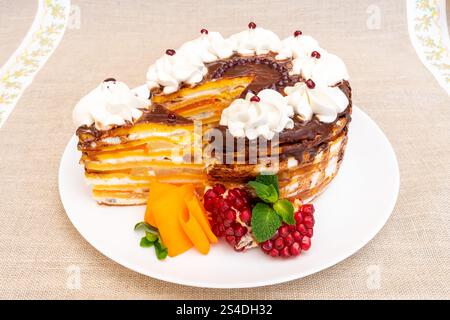 Una torta a strati splendidamente lavorata presenta diversi strati sottili ripieni di panna e glassa di cioccolato. Il dessert è accompagnato da fette di fre Foto Stock