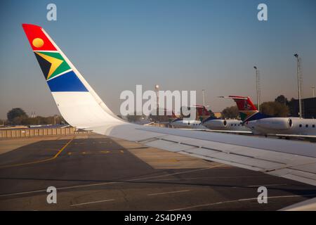 Un'ala di aeroplani delle compagnie aeree sudafricane e tre code di aeroplani Airlink nell'aeroporto internazionale o R Tambo, Johannesburg, Gauteng, Sudafrica Foto Stock