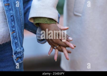 Primo piano di due amici che si tengono per mano, rappresentando un legame profondo e un legame pieno di affetto, fiducia e calore in un ambiente urbano invernale Foto Stock