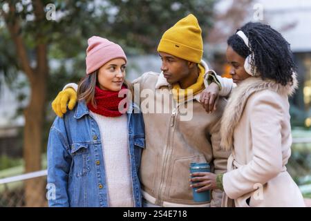 Gruppo di allegri amici multietnici che indossano abiti invernali, camminano insieme in una fredda giornata invernale, divertendosi e chiacchierando Foto Stock