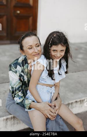 Madre e figlia, 10 anni, seduti insieme su gradini di pietra Foto Stock